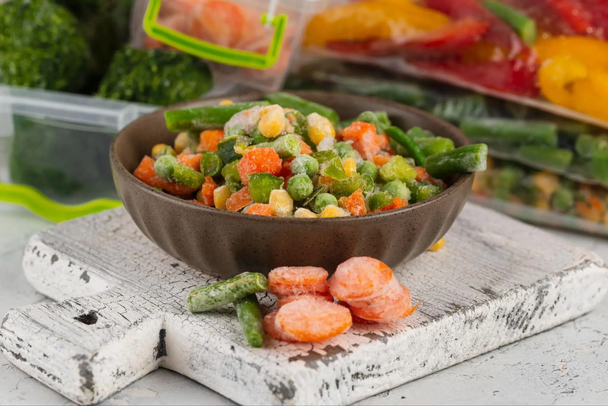 A bowl of frozen mixed vegetables with frozen produce in the background